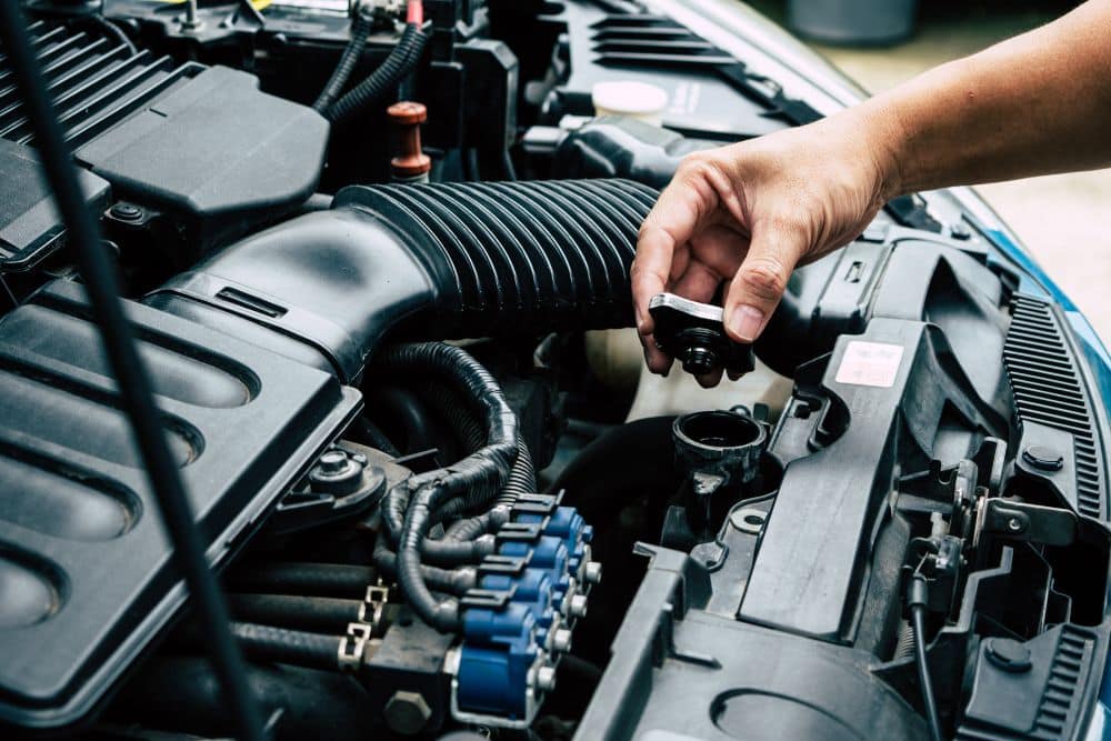 Car maintenance in St. Charles, IL by Precision Motorworks. Mechanic hand removing radiator cap under hood for inspection.