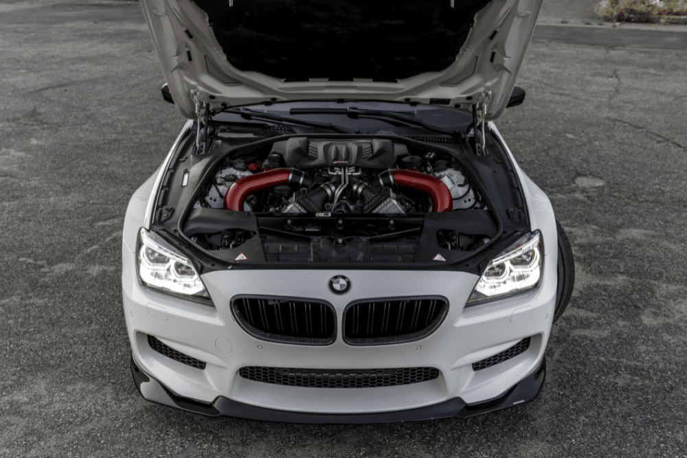 european car care in St. Charles, IL by Precision Motorworks. The image shows a BMW engine bay with red and black tubing, featuring the car’s signature kidney grille and sharp headlights.