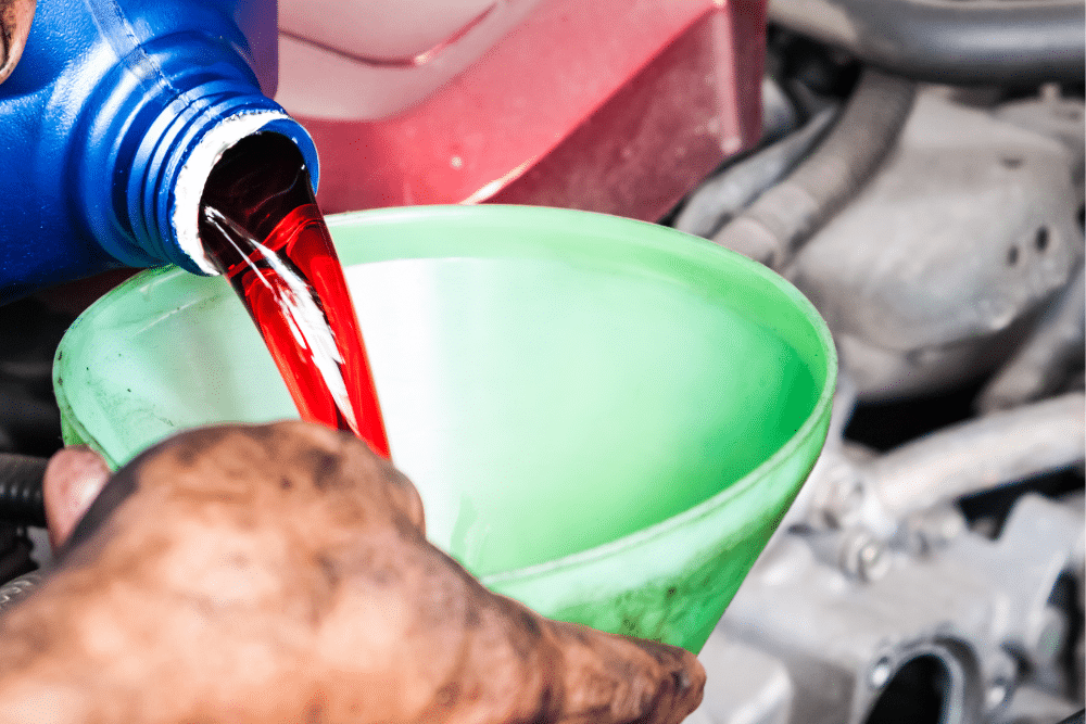 Transmission Fluid in St. Charles, IL by Precision Motorworks. Image of bright red transmission fluid being poured from a bottle into a green funnel under the hood during a fluid service, highlighting proper maintenance and clean fluid handling.